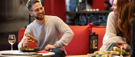 A person sitting on a red couch with a plate of food and a glass of wine on a table.