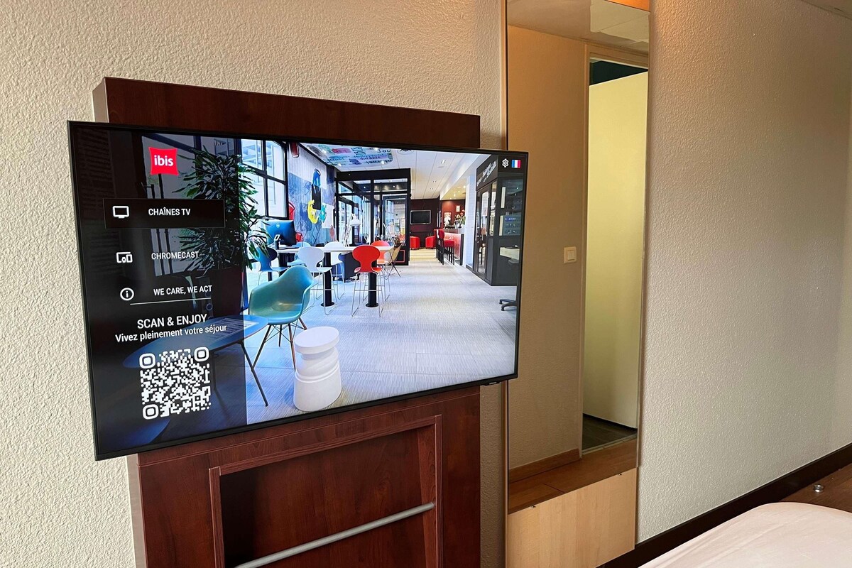 A flat-screen TV mounted on a wooden cabinet with a QR code, displaying a restaurant interior with tables and chairs.