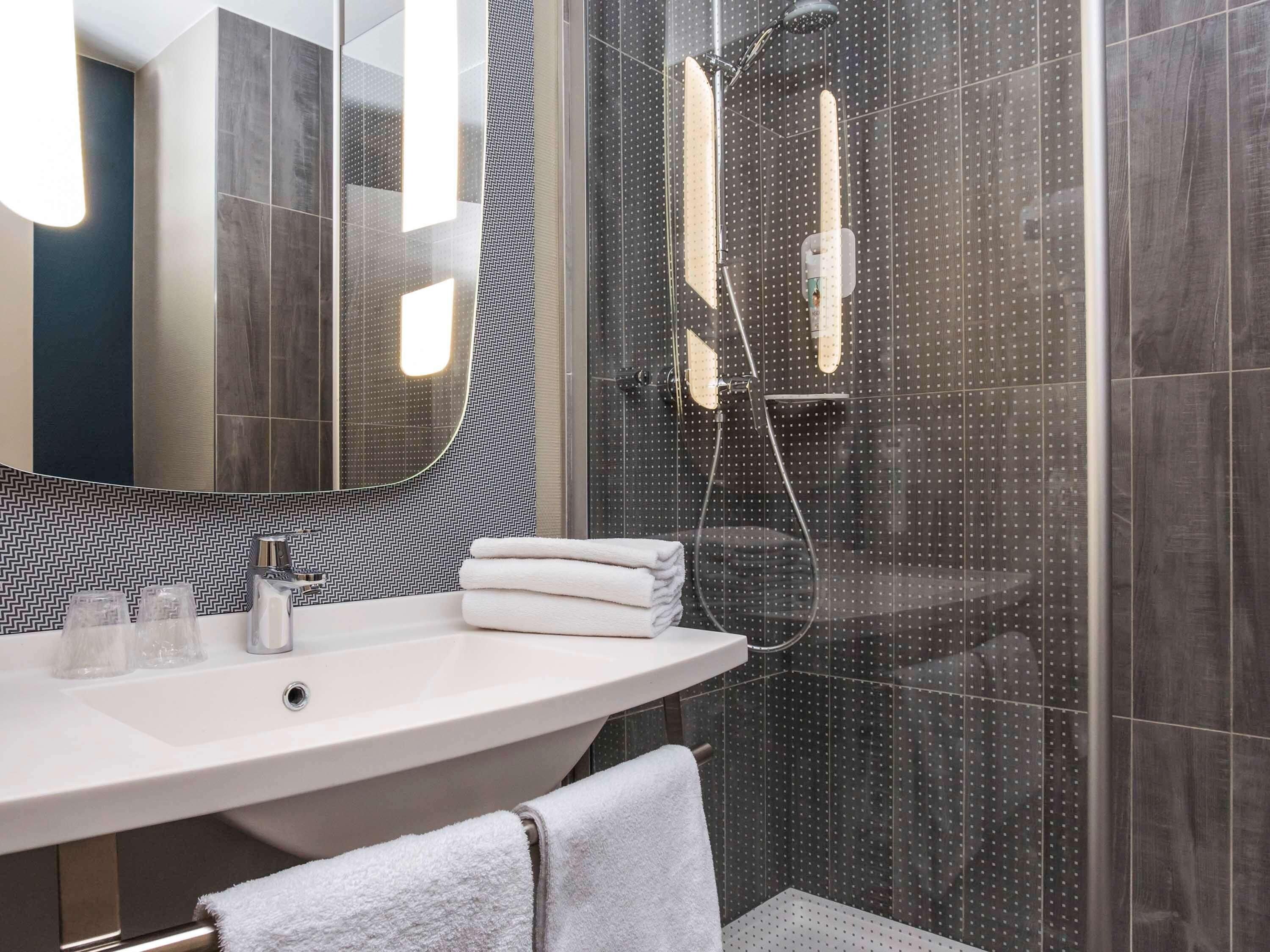 Un baño moderno con un espejo grande, un lavamanos independiente y una zona de ducha con cerramiento de vidrio.