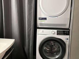 Lavadora de carga frontal con panel de control digital, una secadora encima y una cortina a la izquierda.