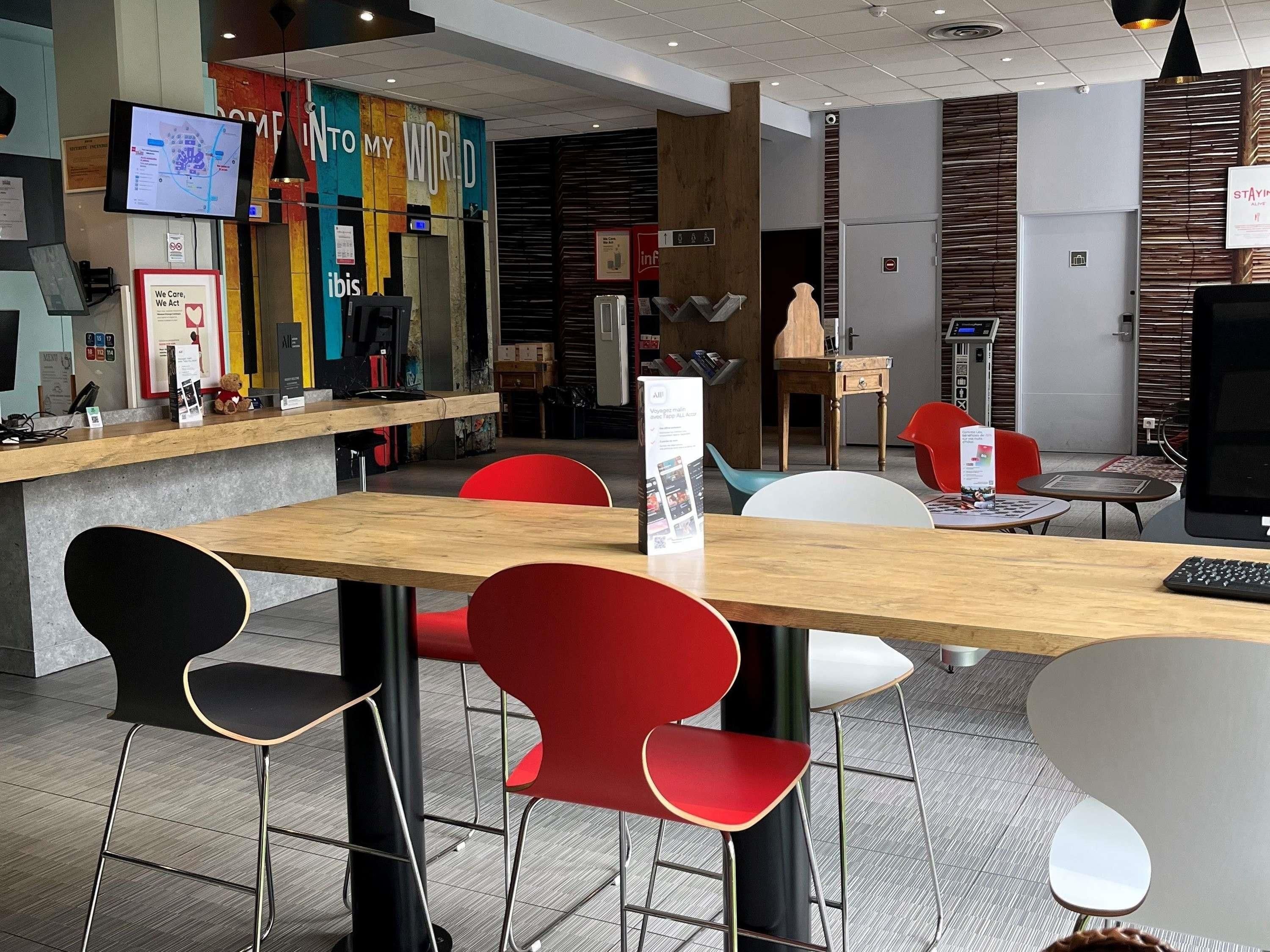 Un intérieur moderne avec un comptoir d’accueil en bois, des chaises rouges et noires, et un écran numérique.