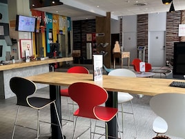 Un interior moderno con un mostrador de recepción de madera, sillas rojas y negras, y una pantalla digital.