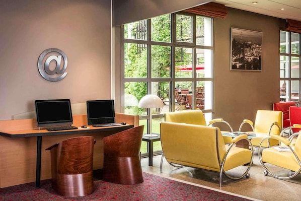 A hotel lobby with two desks, two chairs, a large window, and a cityscape view. - Ibis Villepinte Parc Expos (Villepinte)