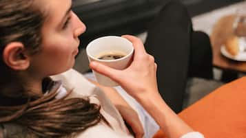 A person holding a cup, seated in a chair with a cushion.