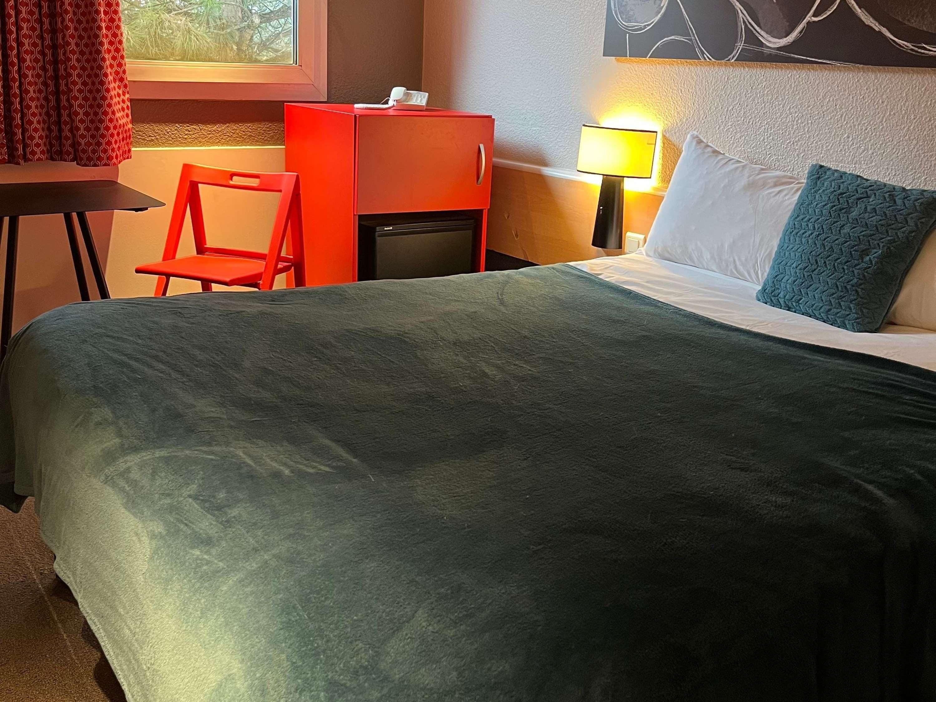 Una habitación de hotel con cama, escritorio, silla, lámpara y ventana.