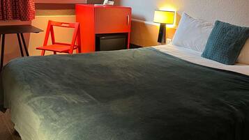 A hotel room with a bed, a desk, a chair, a lamp, and a window.