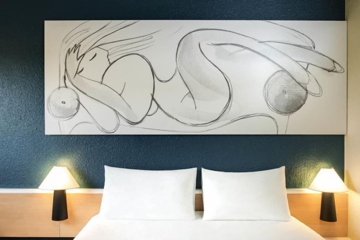 Habitación de hotel con cama, dos lámparas de noche y un cuadro abstracto grande en la pared.
