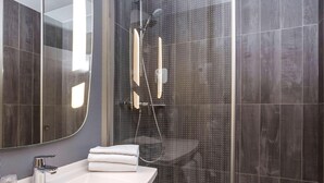 Un baño moderno con ducha de vidrio, un lavamanos blanco y un espejo con un salpicadero de diseño blanco y negro.