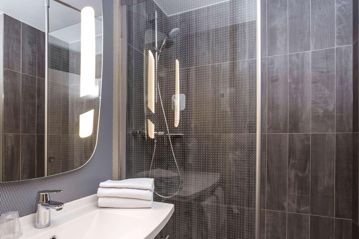 A modern bathroom with a glass-enclosed shower, a white sink, and a mirror with a black and white pattern backsplash.