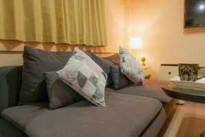 A room with a bed, a bedside table with a lamp, and a television mounted on the wall. - hoshino homestay (Osaka)