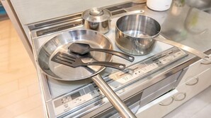 A kitchen with a stainless steel stove, a frying pan, a pot, and a spatula. - hoshino homestay (Osaka)