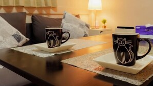 A room with a wooden table, two black mugs with cat designs, a white lamp, and a small plant on a nightstand. - hoshino homestay (Osaka)