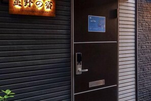 A hotel entrance with a signboard, a door with a keypad lock, and a metal gate. - hoshino homestay (Osaka)