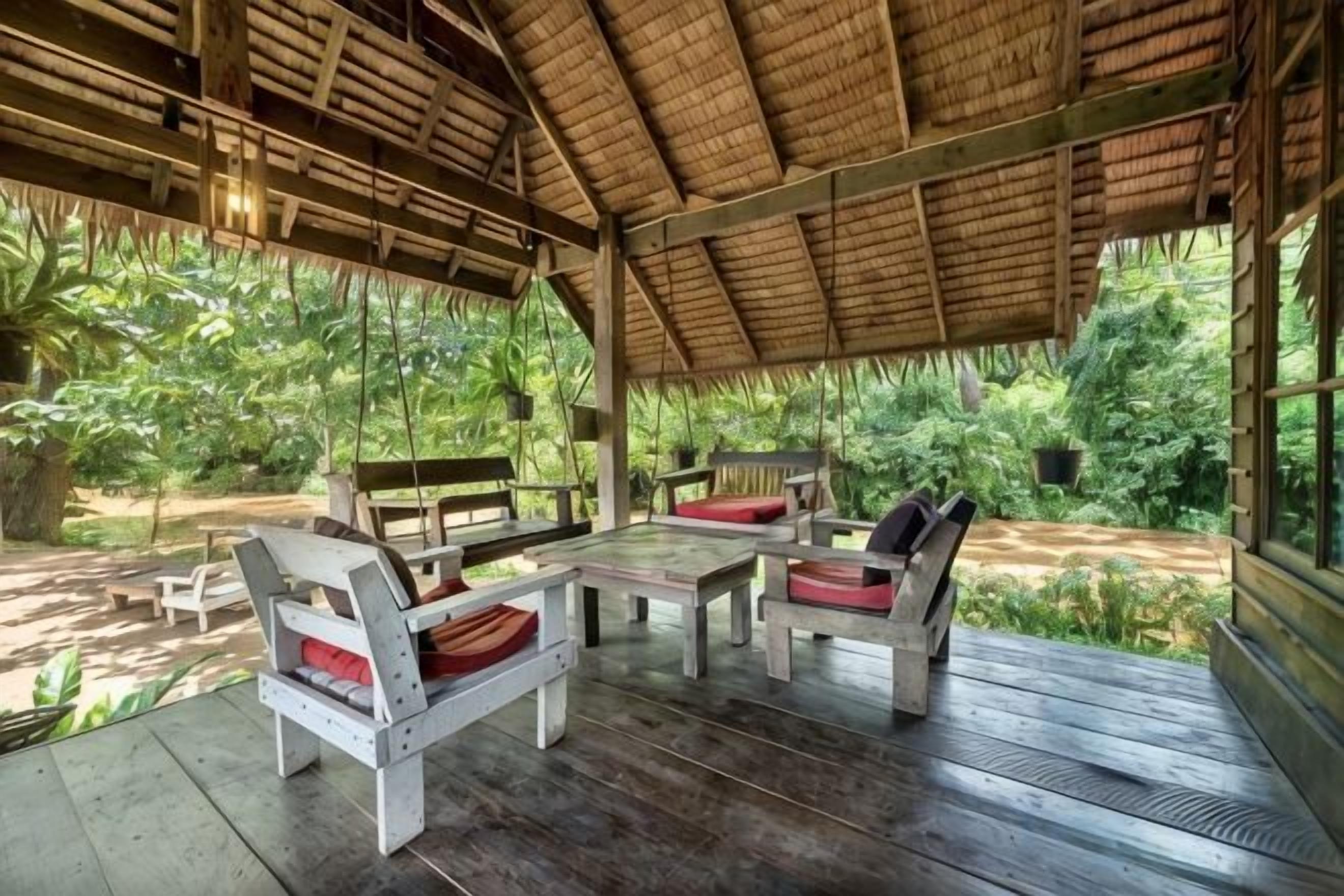 An outdoor covered seating area with wooden furniture and a thatched roof.