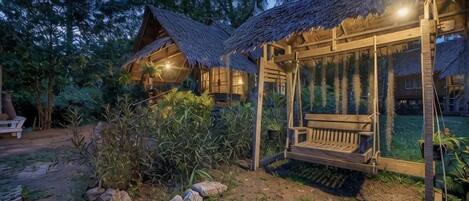 A rustic wooden cabin with a thatched roof, a swing, and a well-maintained garden.