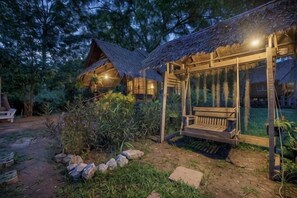 Une cabane en bois rustique, avec un toit de chaume, une balançoire et un jardin bien entretenu.