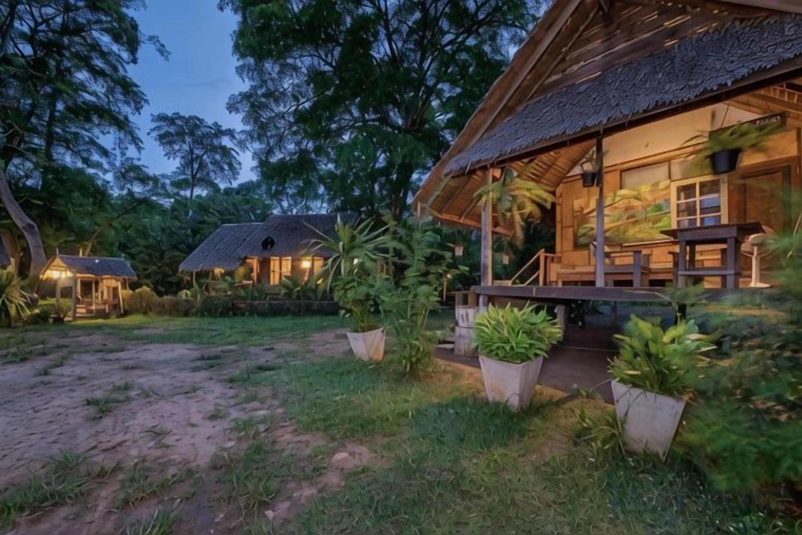 A rustic lodge with a thatched roof, surrounded by lush greenery and potted plants.