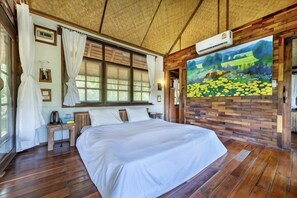 Een slaapkamer met een groot bed, houten vloeren, een raam met gordijnen, een schilderij aan de muur en een airconditioning.