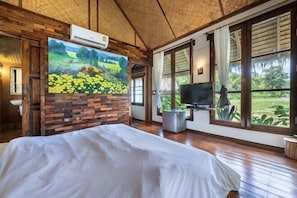 A room with a bed, a painting, a television, and large windows.