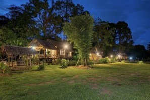 Ein holzgetäfeltes Hotel im Chalet-Stil mit einem Strohdach, umgeben von Bäumen und einer grünen Rasenfläche.