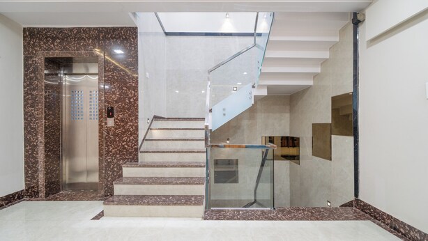 A modern interior with a marble staircase, a glass elevator, and a minimalist design. - Hotel Deol's Paradise (Indore)
