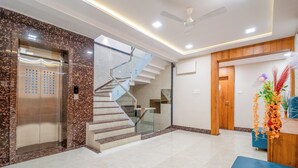 A modern lobby with a marble wall, a glass staircase, a reception desk, and a wooden door. - Hotel Deol's Paradise (Indore)
