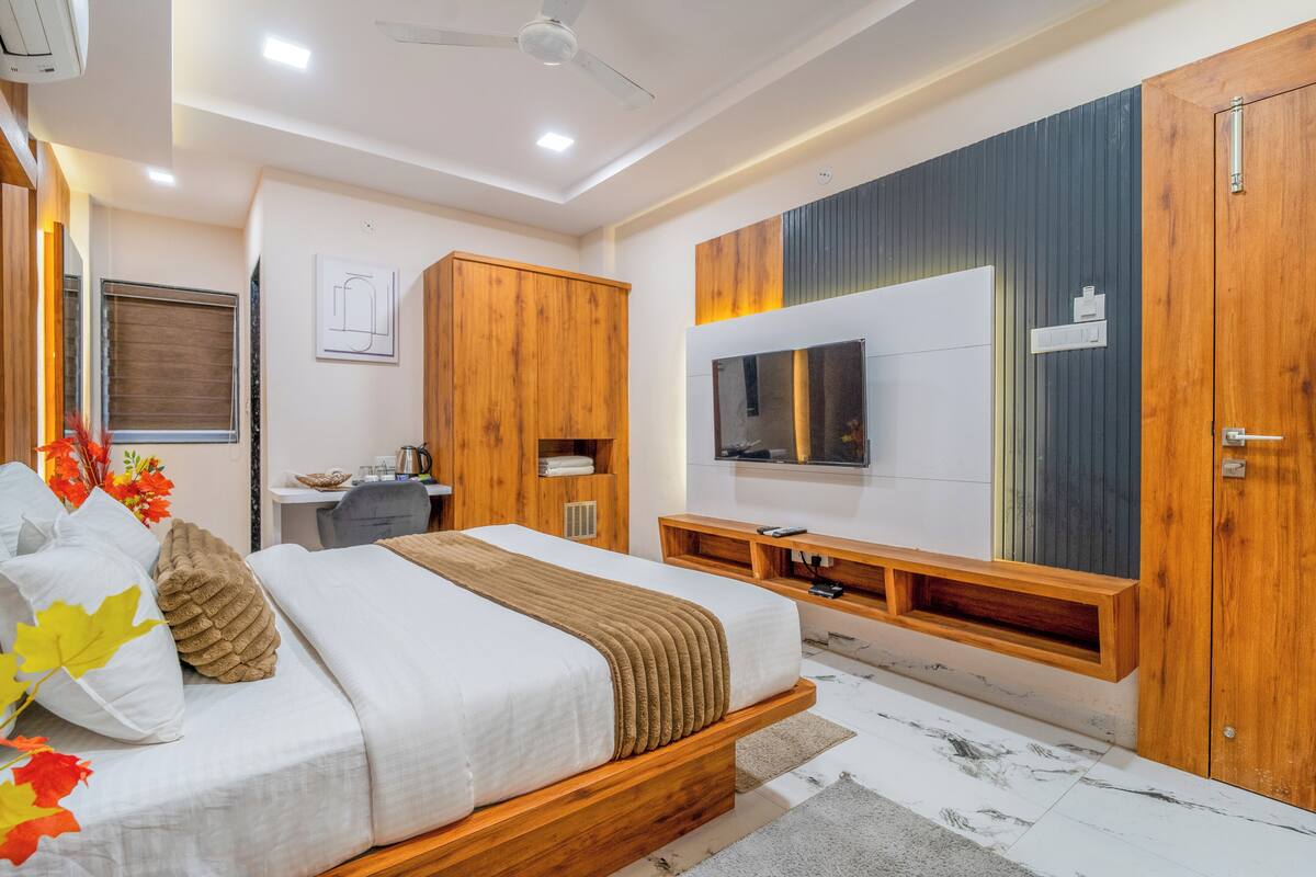 A bedroom with a bed, wooden wardrobe, TV, and a desk with a chair.