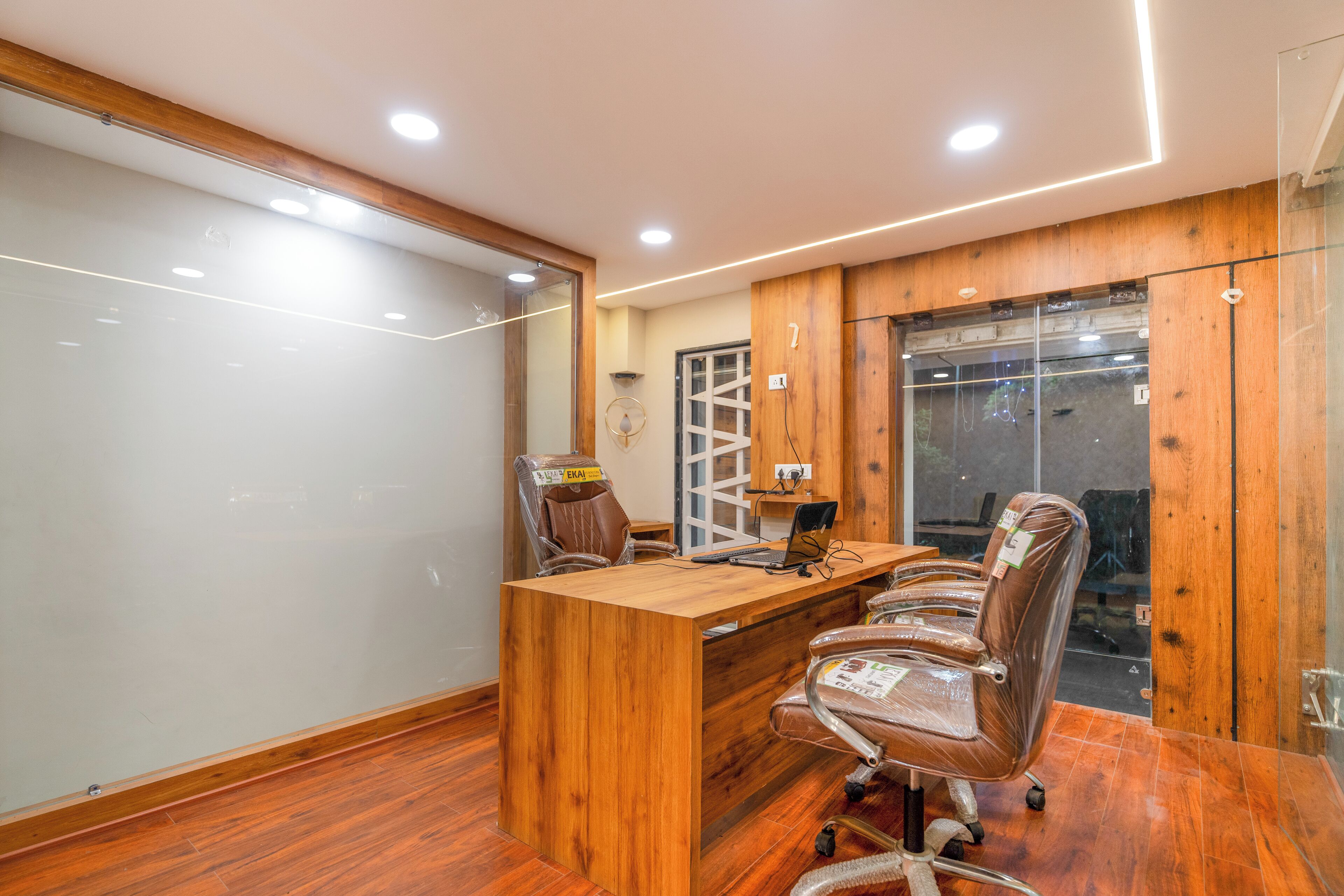 A conference room with a wooden desk, four chairs, a whiteboard, and a glass partition.