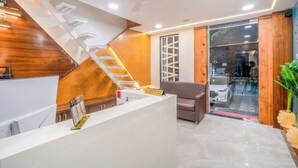 A reception area with a white reception desk, a wooden accent wall, a staircase, a glass door leading outside, and a ceiling fan. - Hotel Deol's Paradise (Indore)