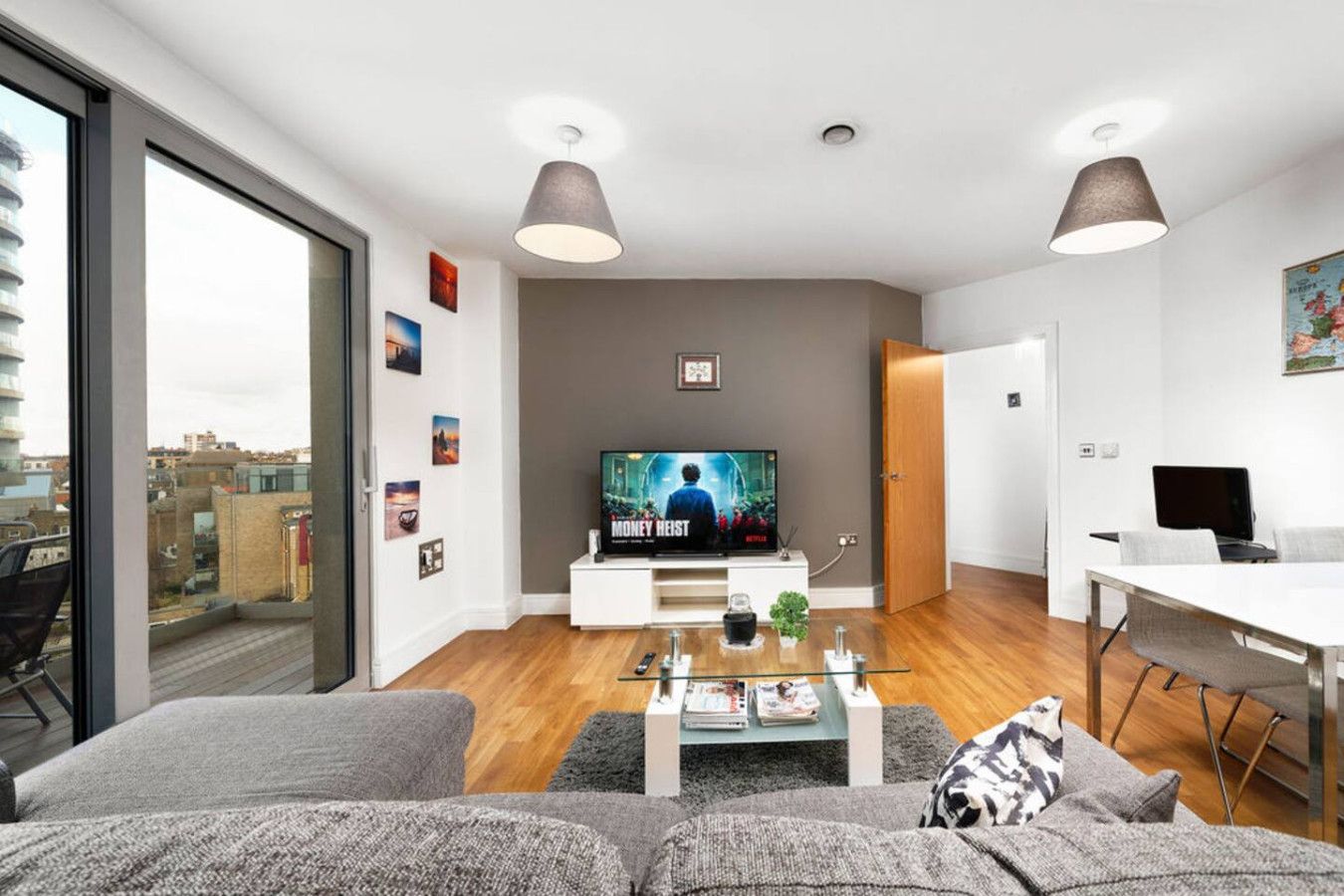 A modern living room with a flat-screen TV, a sofa, a coffee table, and a dining area with a laptop and chair.