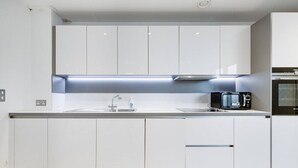 Een moderne keuken met witte kasten, een roestvrijstalen spoelbak, een magnetron en een inbouwoven.