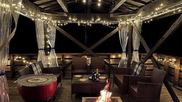 Eine Terrasse im Freien mit Korbmöbeln, einem Feuerkorb und Lichterketten.