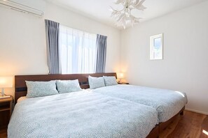 A double bed with a patterned bedspread, a wooden headboard, a nightstand with a lamp, a window with curtains, and a framed picture on the wall.