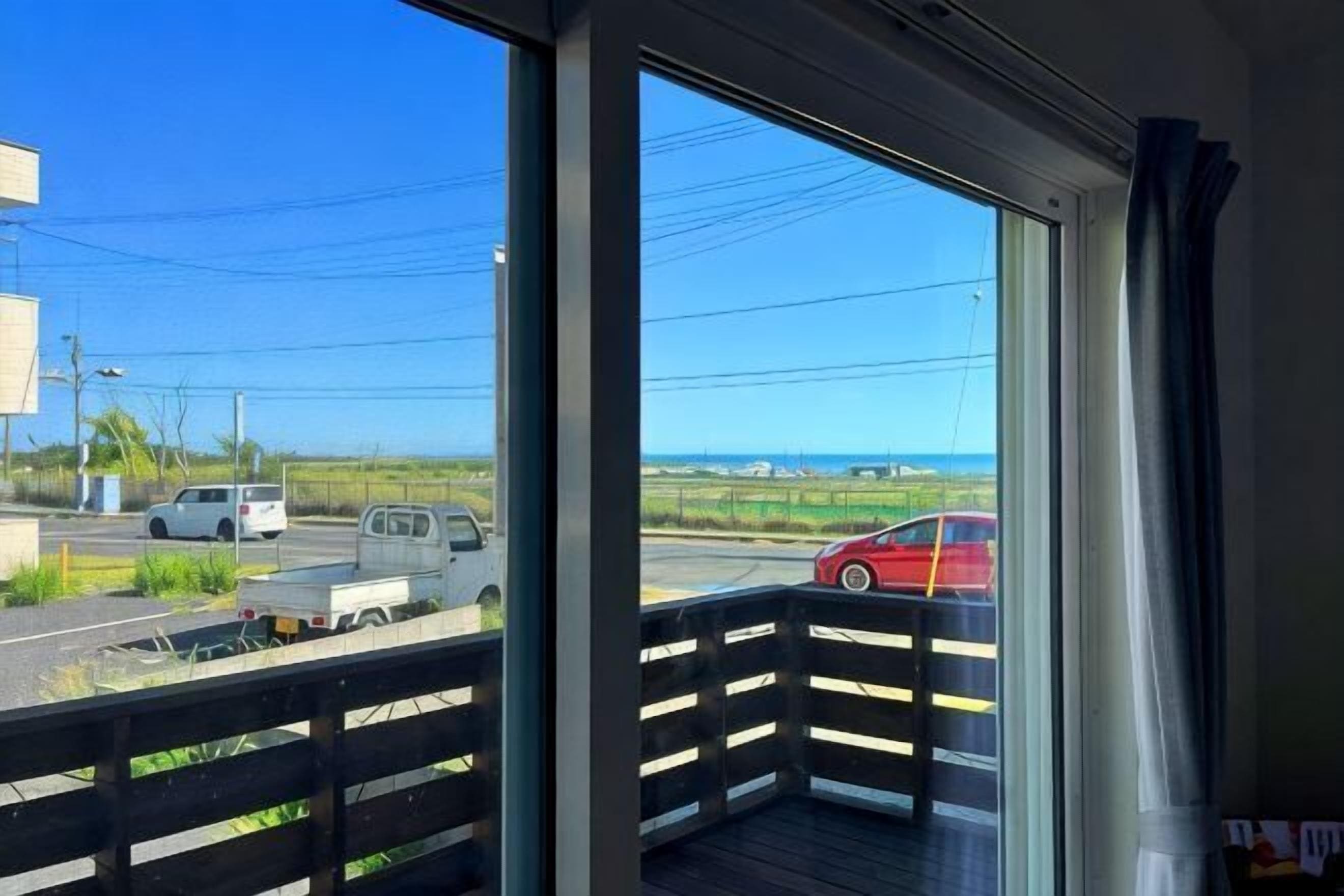 A balcony with a view of a road and a red car, a clear sky, and a distant landscape.