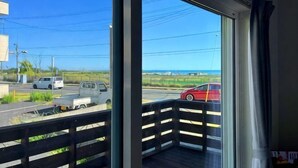 A balcony with a view of a road and a red car, a clear sky, and a distant landscape. - KandoStay Kujyukuri SORA Terrace (Ichinomiya)