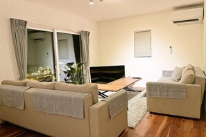 Un salon comprenant un canapé, une petite banquette, un téléviseur et une table à manger.
