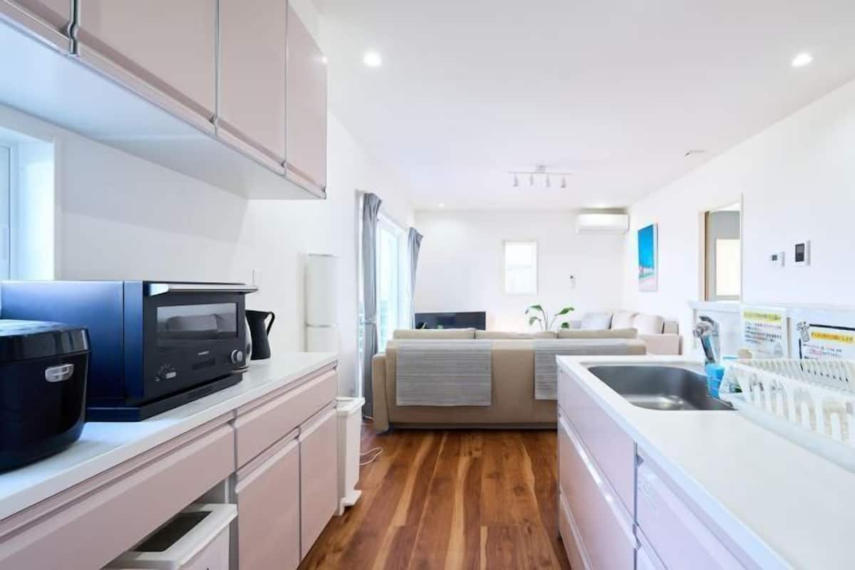 A modern kitchen with a microwave, coffee maker, and sink. There is a sofa in the background and a window with curtains.
