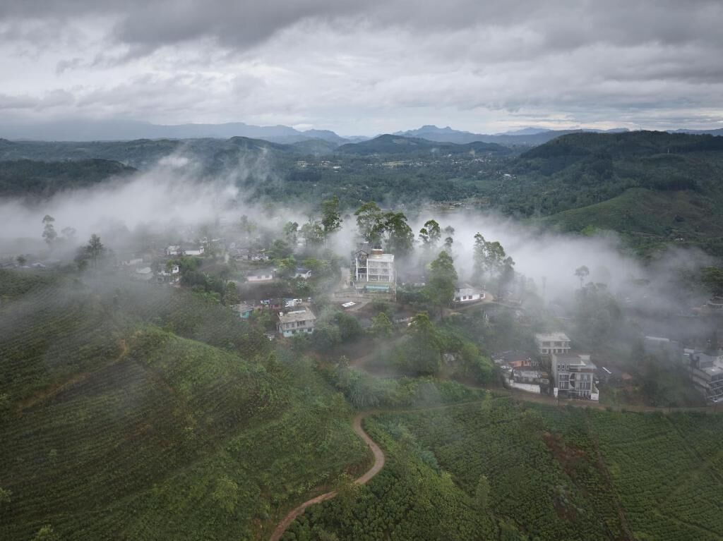 Paisaje rural con edificios dispersos en medio de abundante vegetación y colinas cubiertas de niebla.