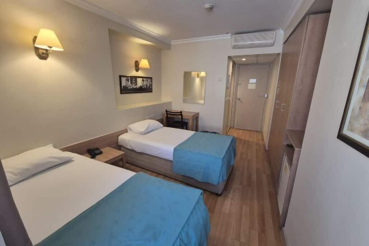 A hotel room with two single beds, a desk, a chair, a small table, and a mirror.