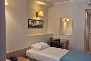 A hotel room with a bed, bedside table, lamp, chair, desk, and a mirror.