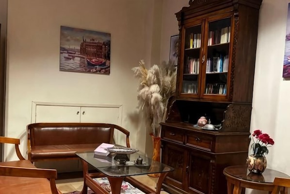 A living room with a brown leather sofa, a glass coffee table, a wooden cabinet, and a bookshelf.