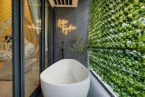 Ein modernes Badezimmer mit einer weißen Badewanne, einer Glasduschtür und einer grünen Wand mit vertikalem Garten.