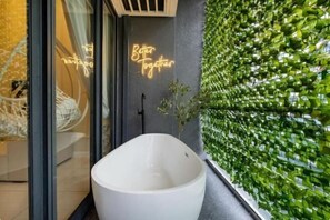 A modern bathroom with a white bathtub, a glass shower enclosure, and a green vertical garden wall. - ELEMENT BY FEEL HOME(The elements@Ampang) (Kuala Lumpur)