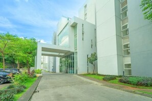 A modern building with a glass entrance and a paved walkway. - DREAM INN Aeropolis By Reccoma (Neglasari)