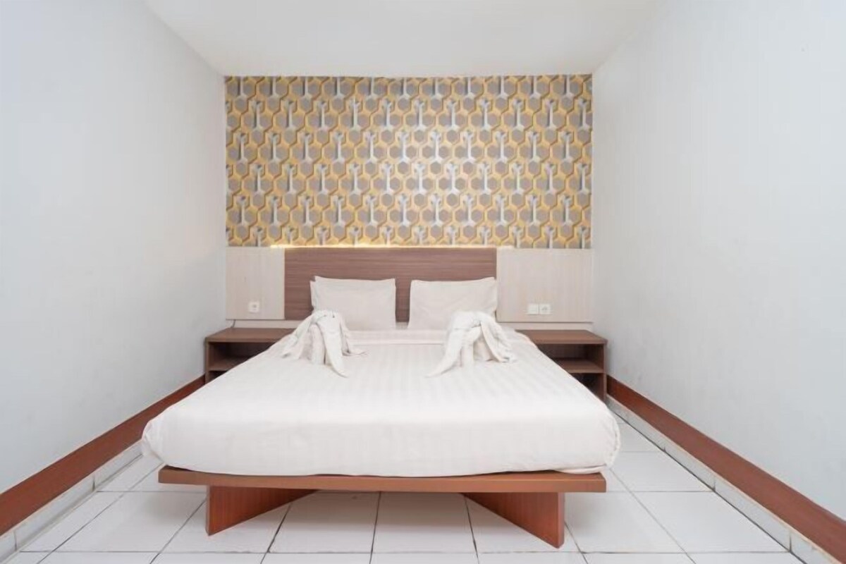 A modern hotel room with a large bed, wooden headboard, and a patterned wall design.