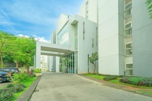 A modern building with a covered entrance, a paved driveway, and a landscaped garden area. - DREAM INN Aeropolis By Reccoma (Neglasari)