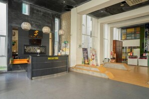 Un espace d'accueil comprenant un comptoir de réception, un mur noir orné d'une enseigne et un escalier menant à un niveau supérieur.
