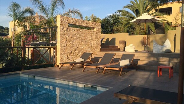 A poolside area with lounge chairs, a stone wall, and a view of the surrounding landscape.