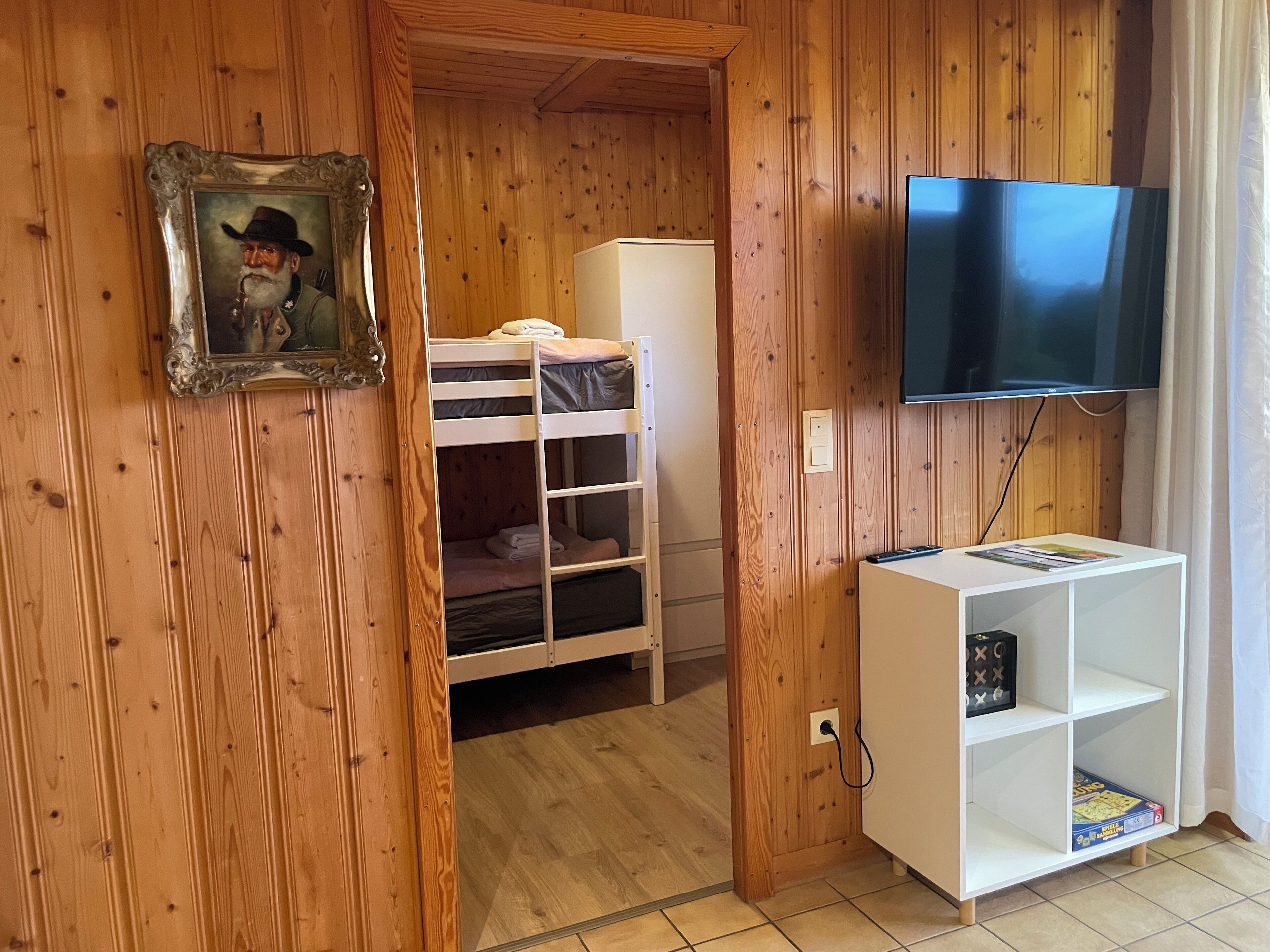 Ein Zimmer mit Holzwandverkleidung, einem Etagenbett, einem Fernseher und einer weißen Regalwand.