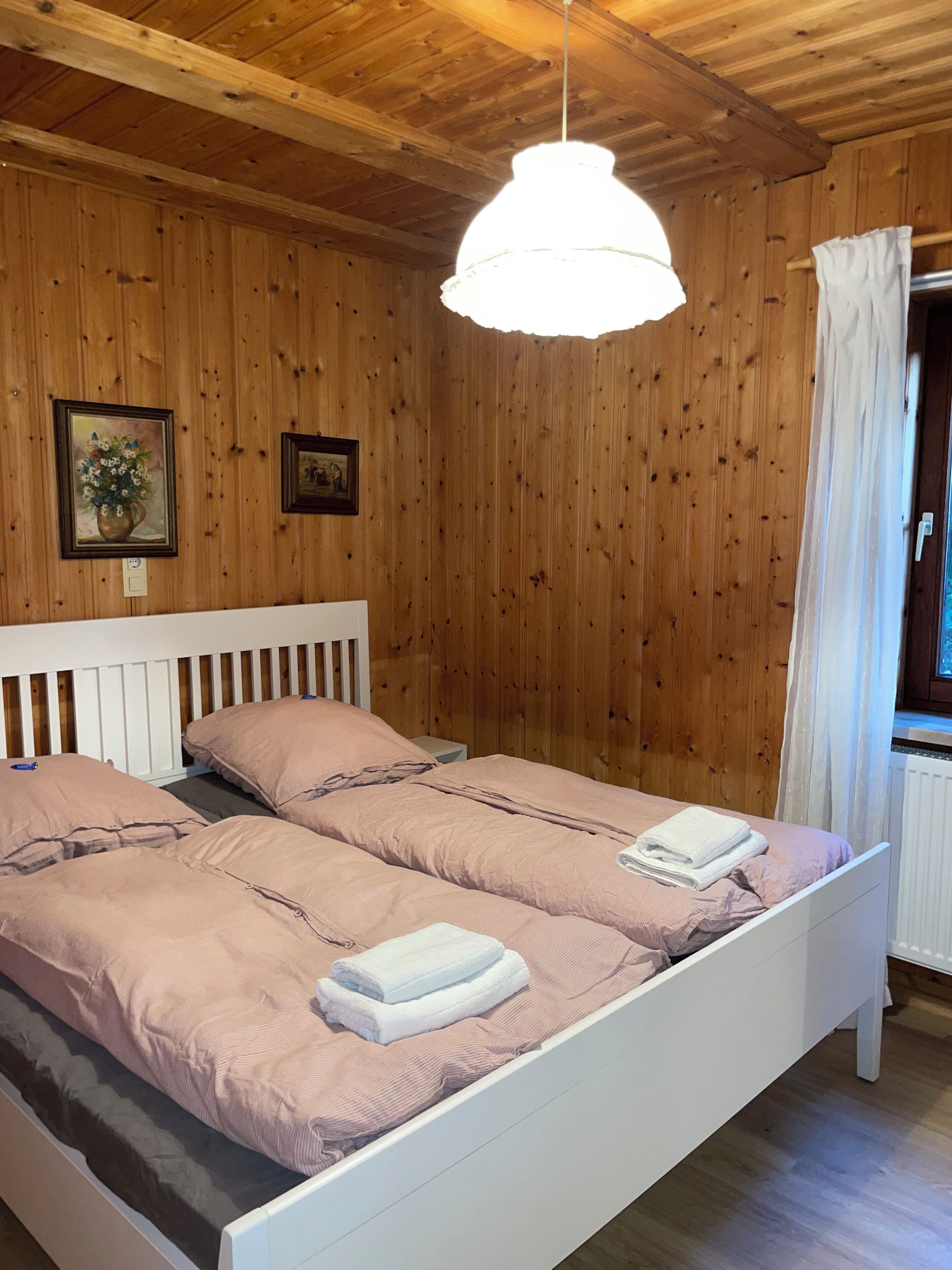 A wooden-paneled room with a bed, a hanging light fixture, and a window with curtains.